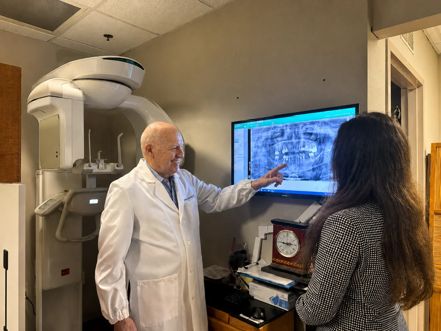 Dr. Maxson reviewing a 3D cone-beam CT scan with a team member on a monitor next to the CBCT scanner